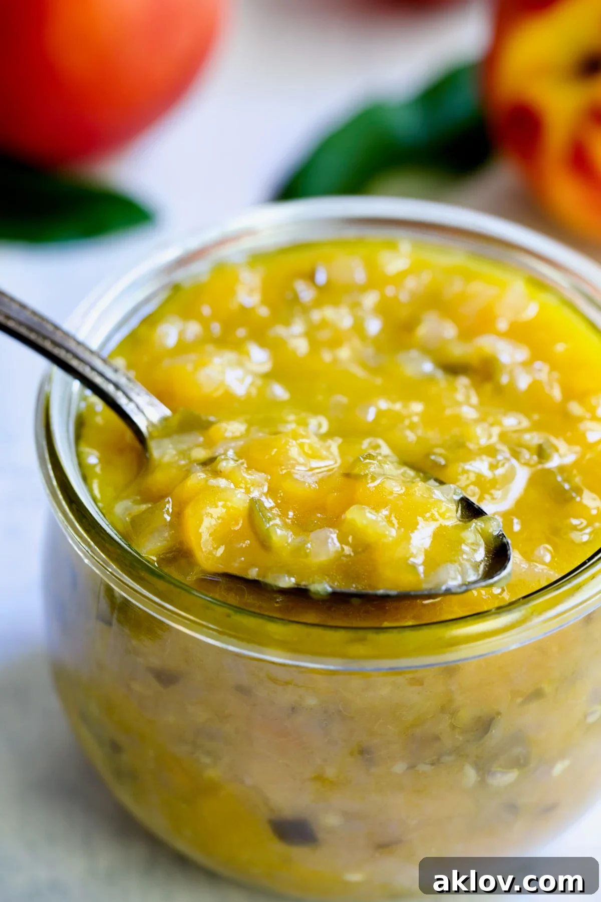 A close-up view of the chunky texture of Peach Jalapeno Chutney in a glass jar, with a spoon showcasing its beautiful consistency.