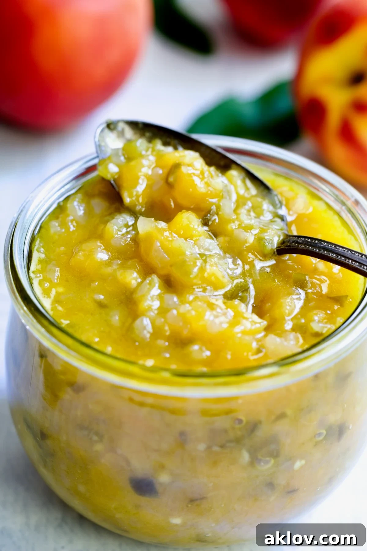 A beautifully presented glass jar of Peach Jalapeno Chutney with a spoon, ready to be served or stored.