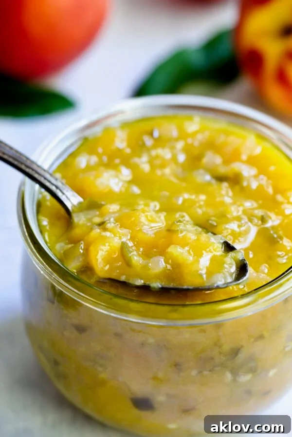 Peach Jalapeno Chutney in a glass jar with a spoon holding some to show detail.
