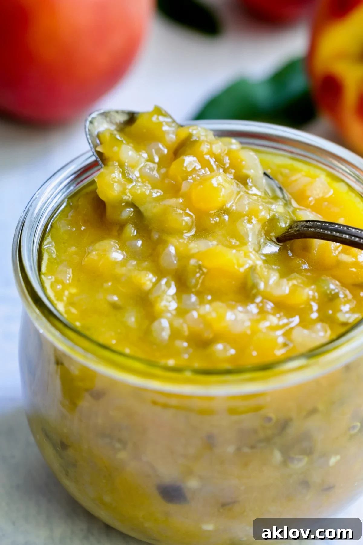 Close-up shot of Peach Jalapeno Chutney in a clear glass jar, with a small spoon scooping some out, highlighting the chunky texture.