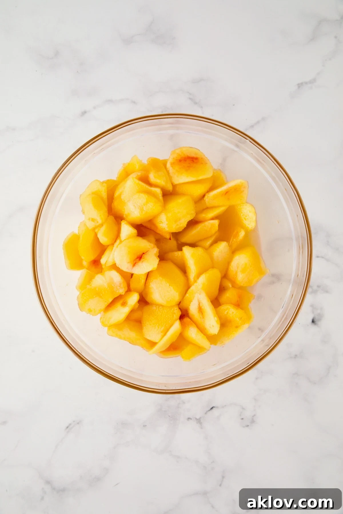 Freshly peeled peach chunks soaking in a bowl of club soda to prevent browning.