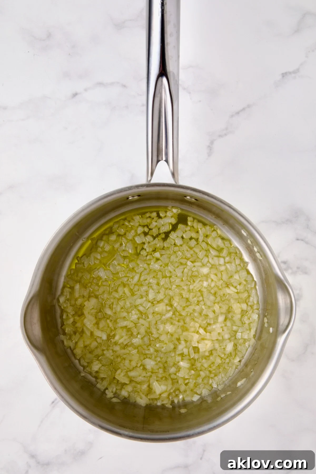 Finely chopped onion cooking in olive oil in a stainless steel saucepan.