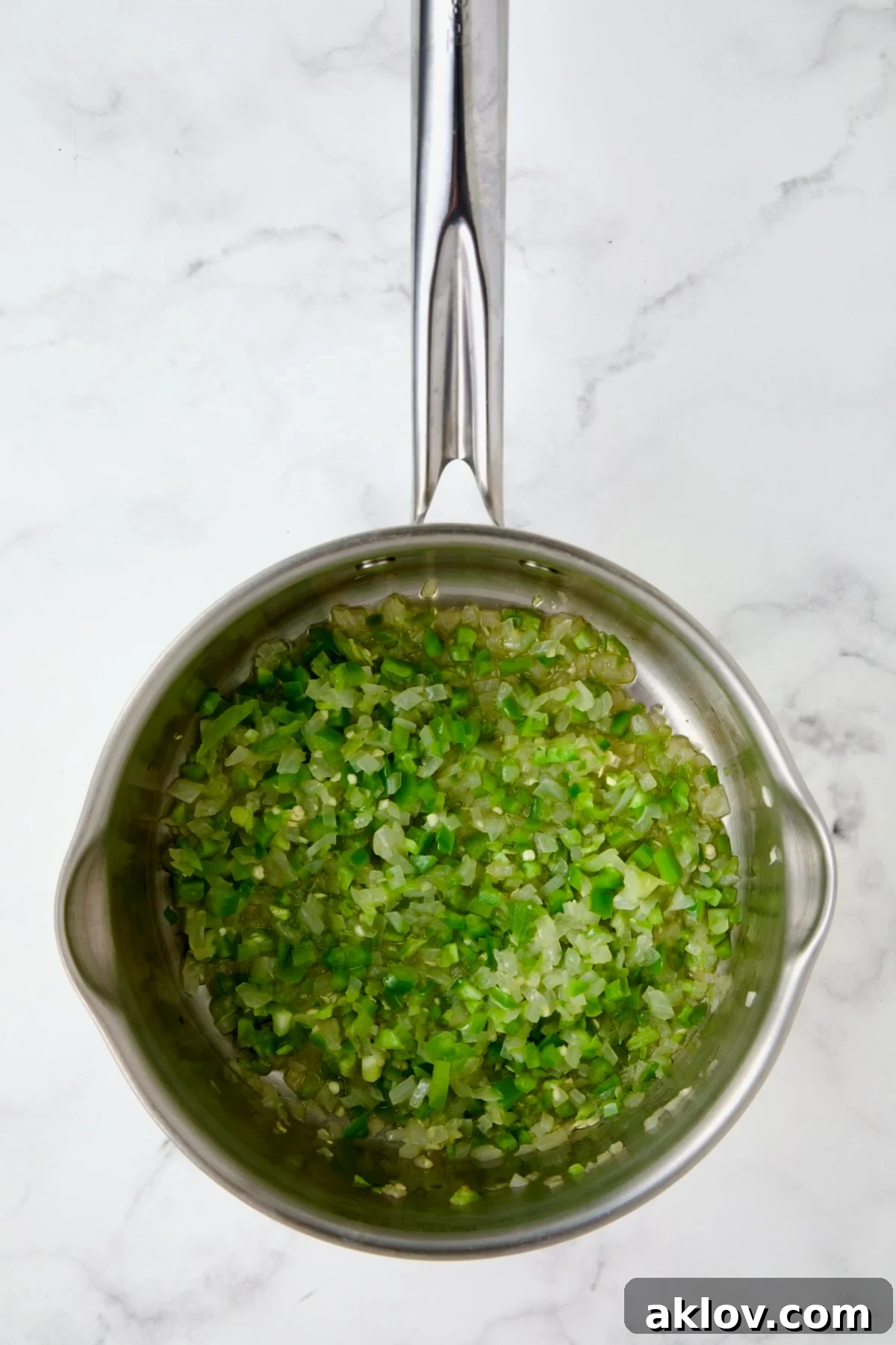 Sautéed onion, chopped jalapeño, and minced ginger cooking in olive oil in a stainless steel saucepan.