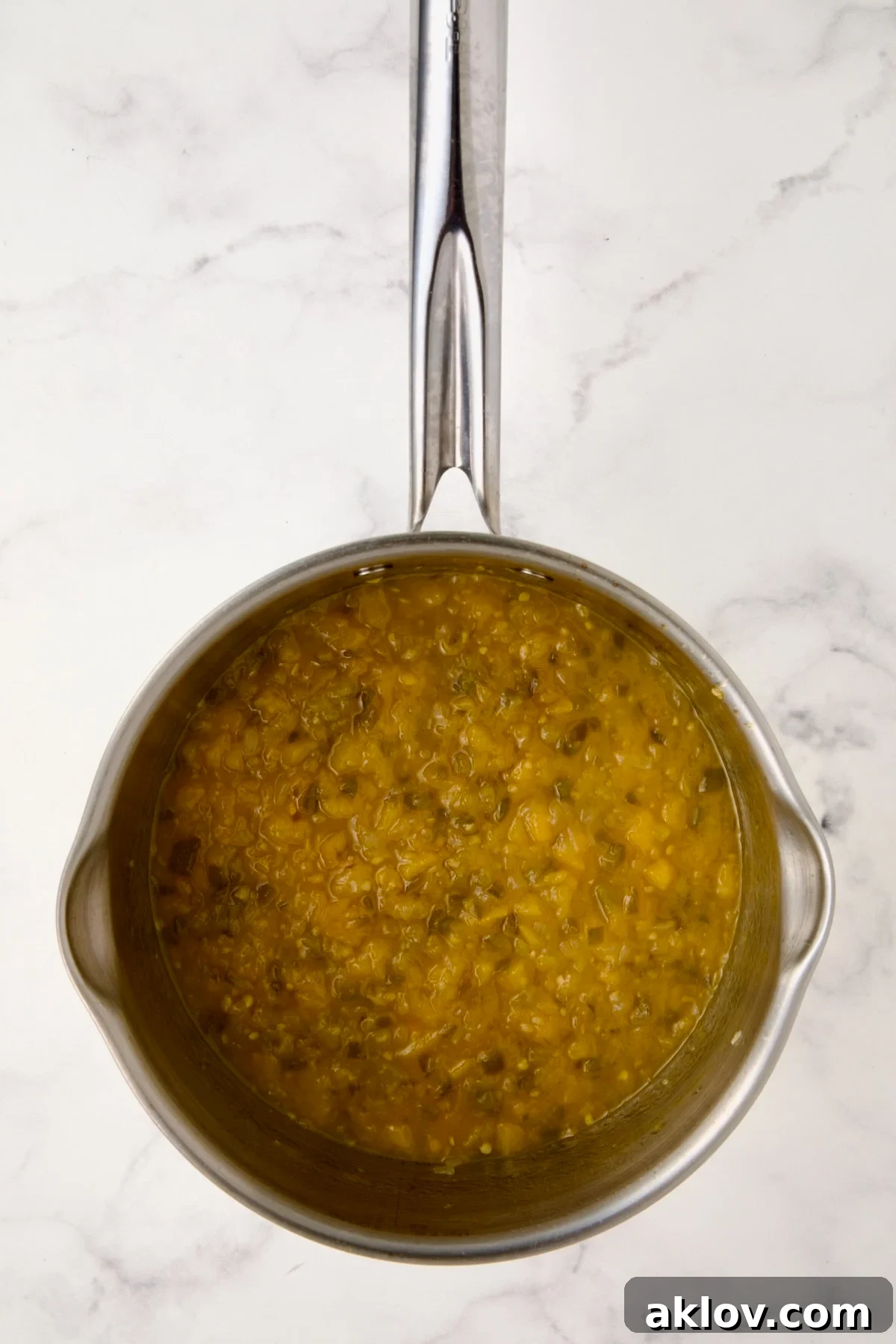 Thickened, jam-like Peach Jalapeno Chutney simmering in a stainless steel saucepan, indicating it's nearly ready.