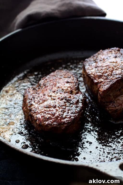 Photo of two perfectly seared beef tenderloin fillets in a cast iron skillet, showcasing a deep brown crust.