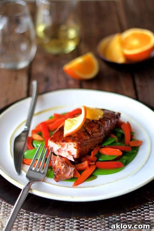 Photo of Pomegranate and Orange-Glazed Salmon with Stir-Fried Vegetables on white plate with salmon cut into.
