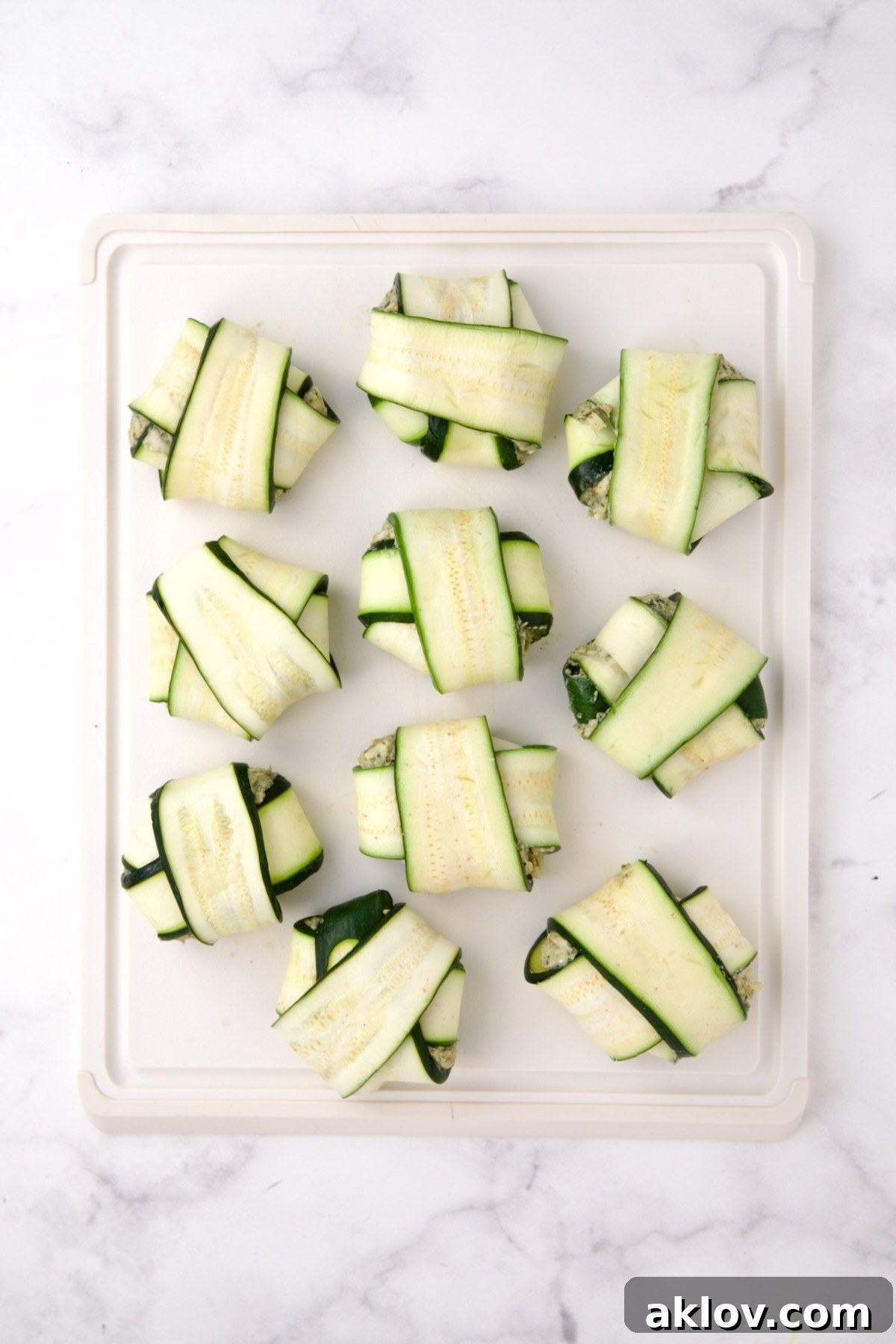 Ten fully assembled zucchini ravioli on white cutting board.