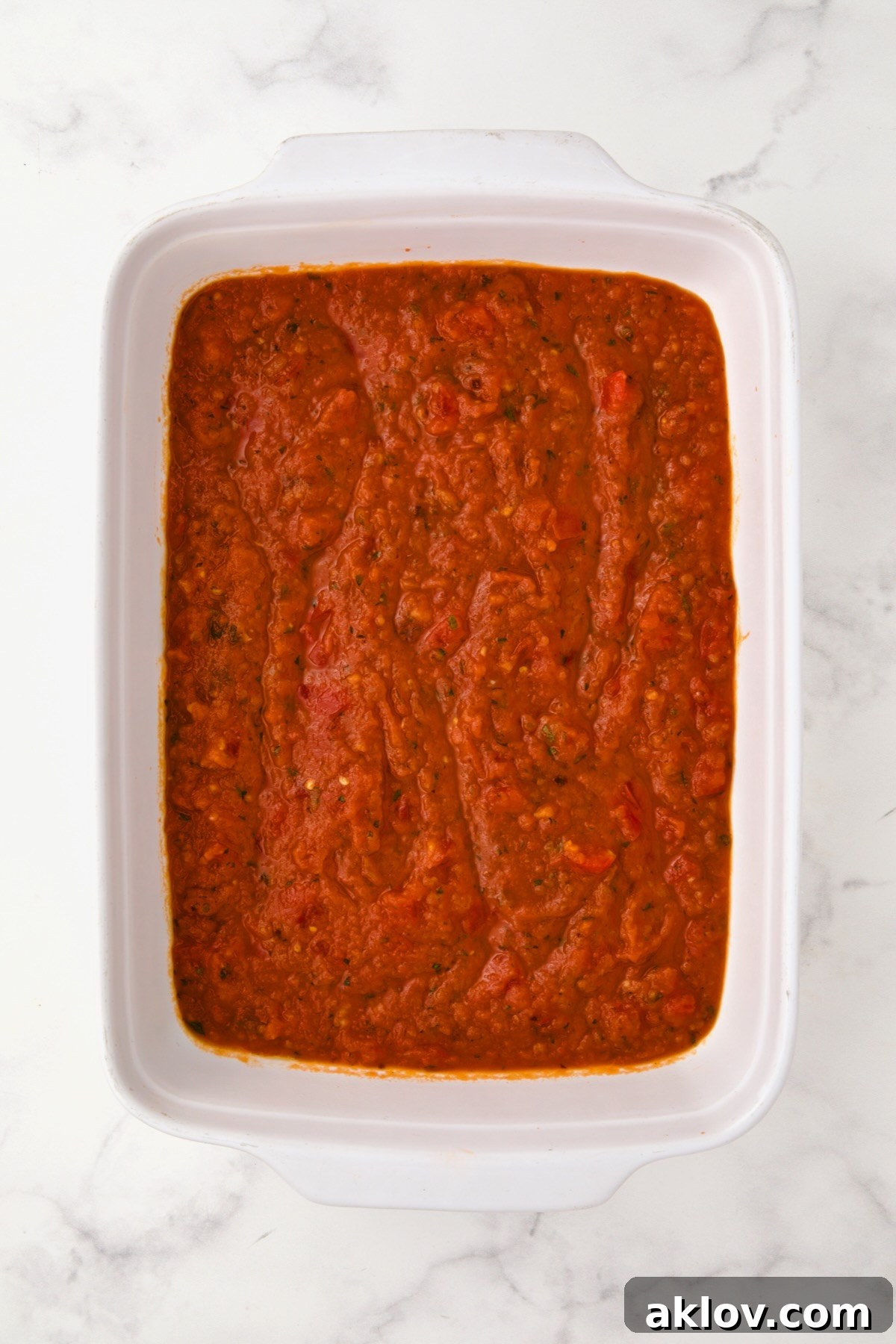 Marinara sauce in the bottom of a rectangular white ceramic baking dish.