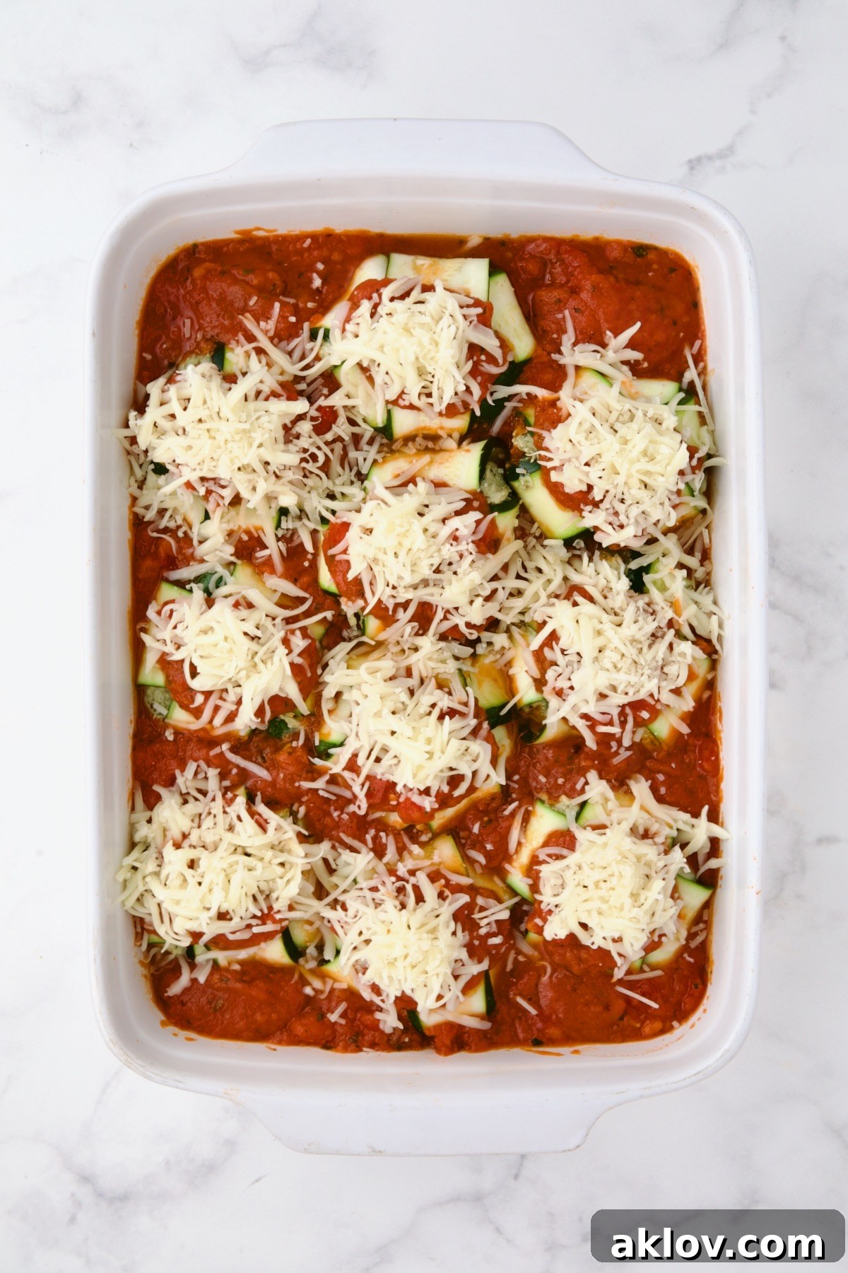 Fully assembled zucchini ravioli with cheese added before being baked in rectangular white ceramic baking dish.