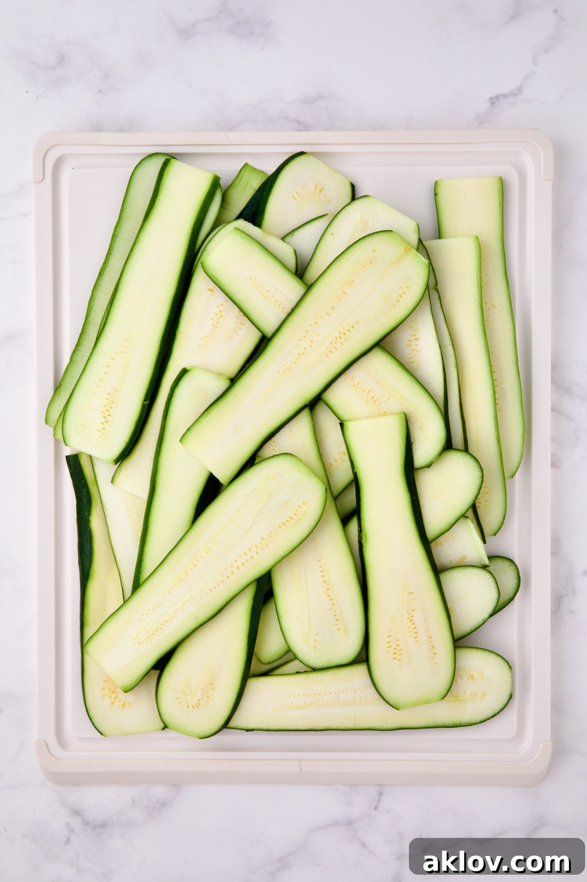 Thinly sliced zucchini on white cutting board.