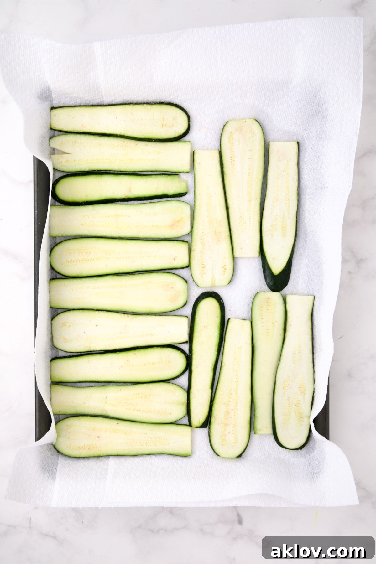 Thinly sliced salted zucchini slices on paper towel lined baking sheet.