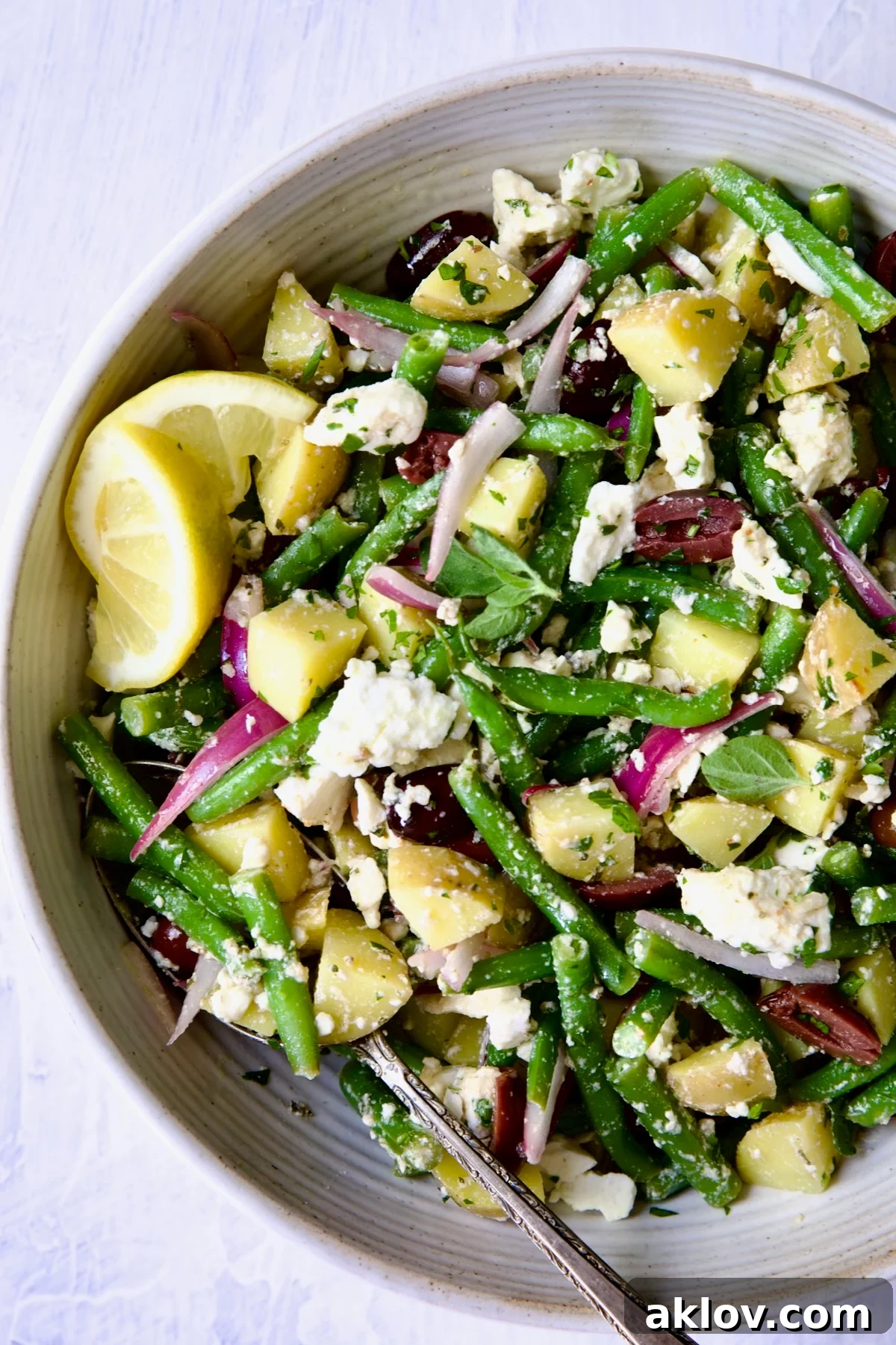 The vibrant Potato Green Bean Salad, elegantly presented in a white bowl, garnished with fresh lemon wedges that hint at its zesty flavor profile.