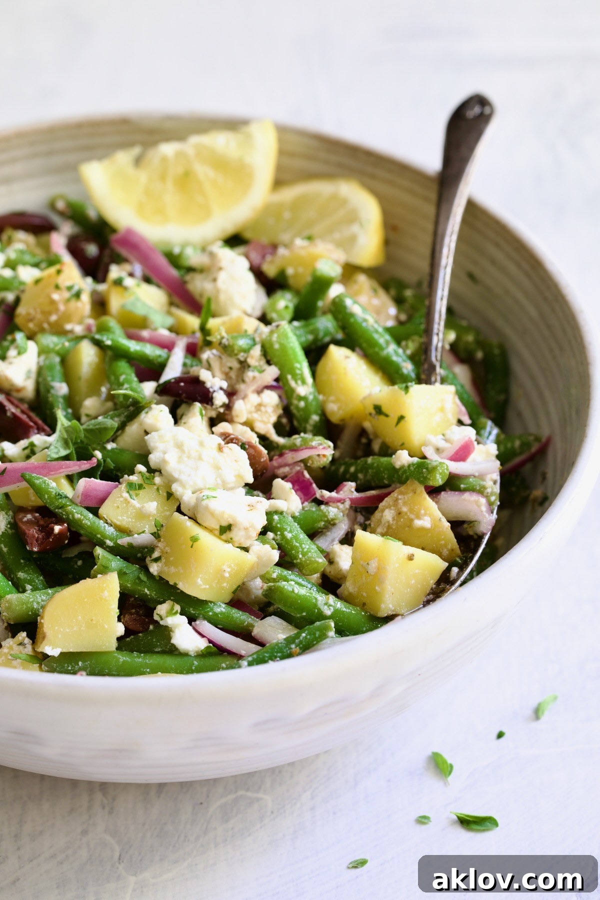 A pristine white bowl filled with the inviting Potato Green Bean Salad, accompanied by a serving spoon, highlighting its readiness to be enjoyed.