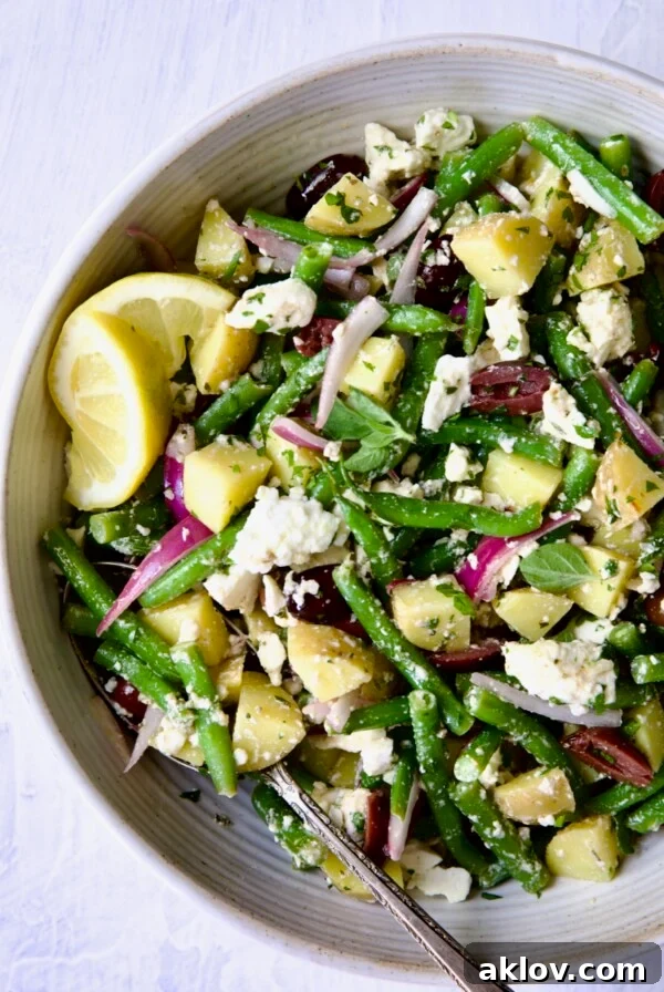 Potato Green Bean Salad in white bowl with lemon wedges.