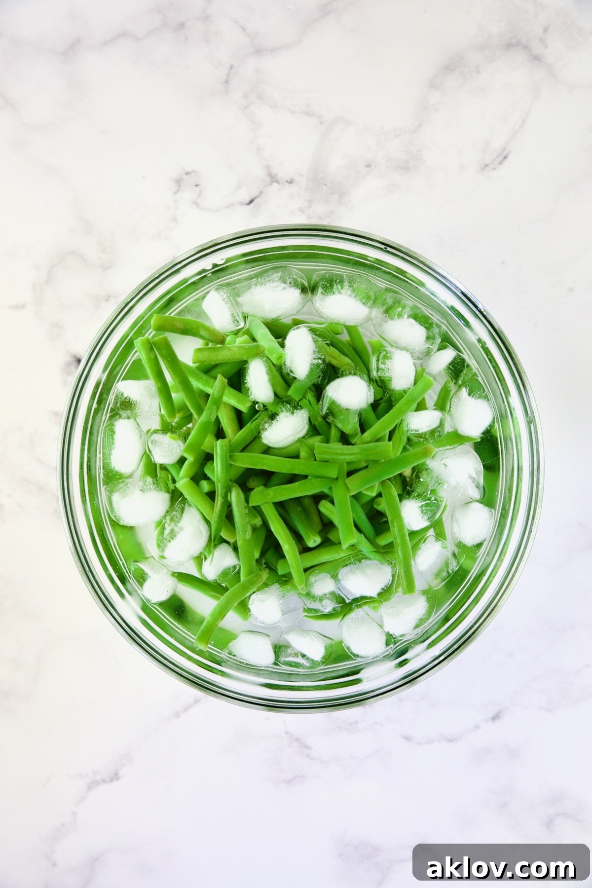 Freshly blanched green beans submerged in a refreshing ice bath in a clear glass bowl, showcasing their vibrant green color.