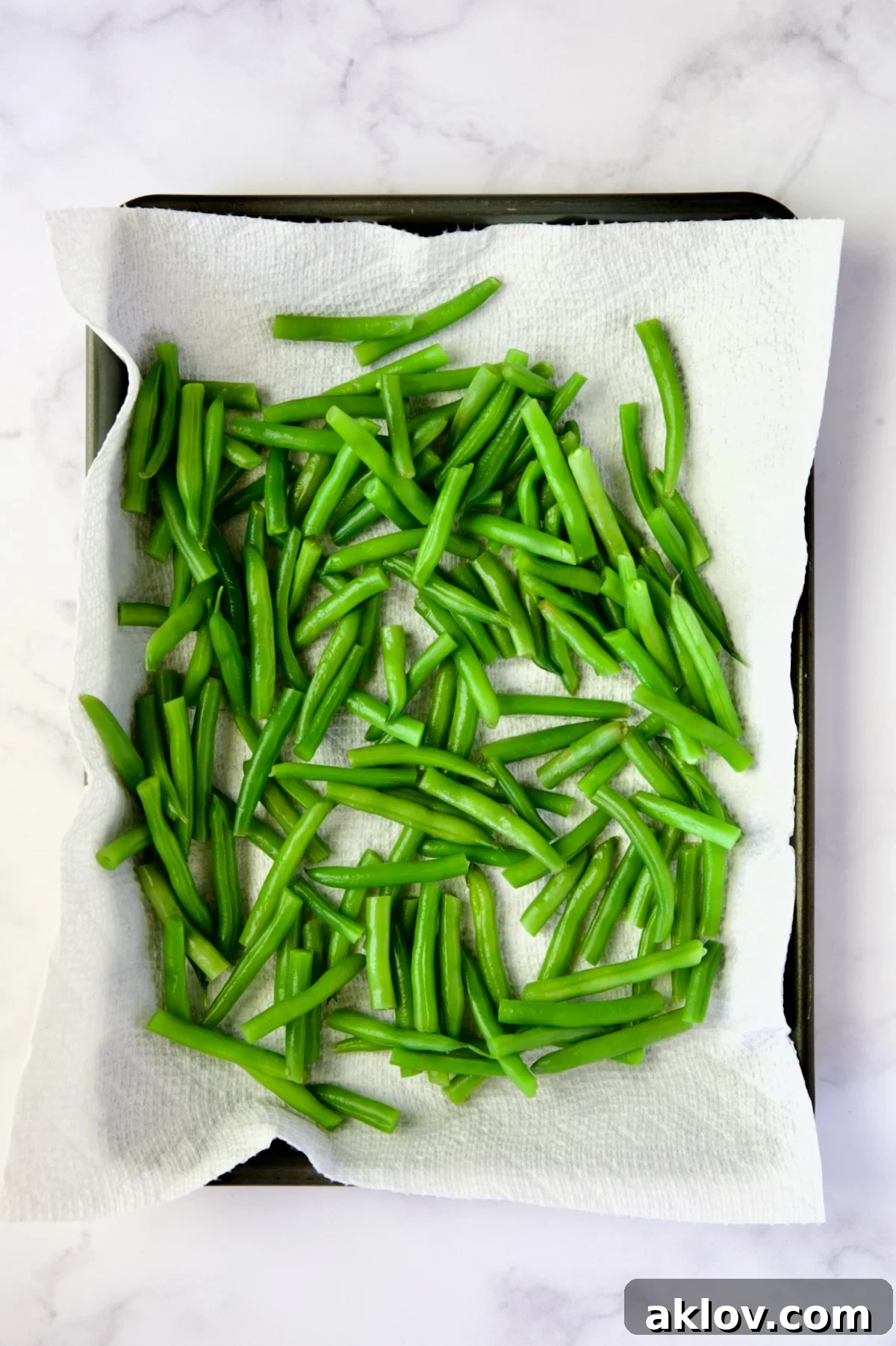 Blanched green beans meticulously arranged on a paper towel-lined rimmed baking sheet, ready for the next step in the salad preparation.