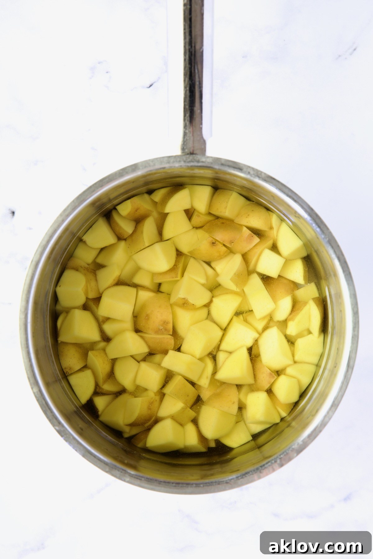 Cubed Yukon Gold potatoes simmering in salted water within a gleaming stainless steel saucepan, preparing for a tender finish.