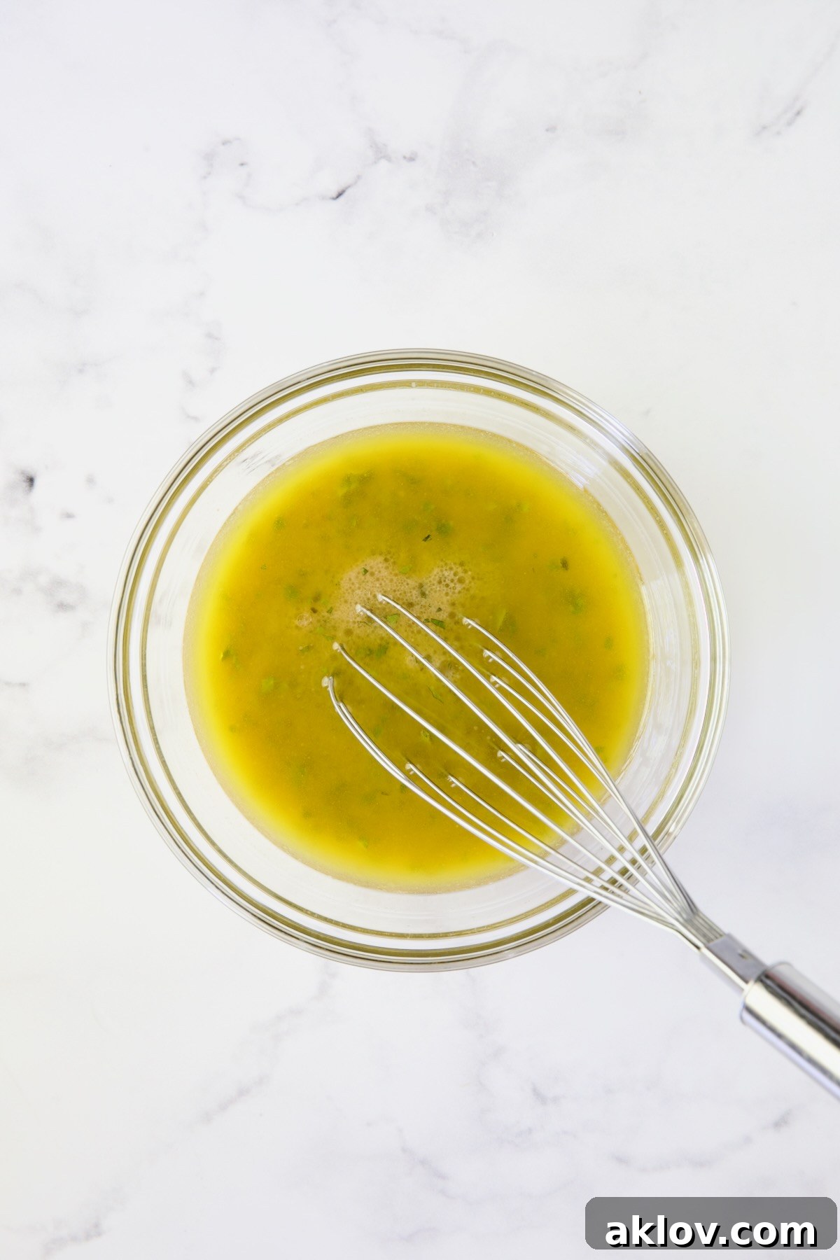 A zesty vinaigrette being vigorously whisked with a wire whisk in a small bowl, creating a perfectly emulsified dressing.