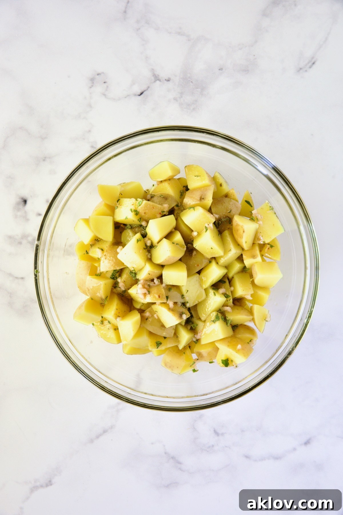 Cooked Yukon Gold potatoes glistening with vinaigrette in a clear glass bowl, cooling down while absorbing rich flavors.