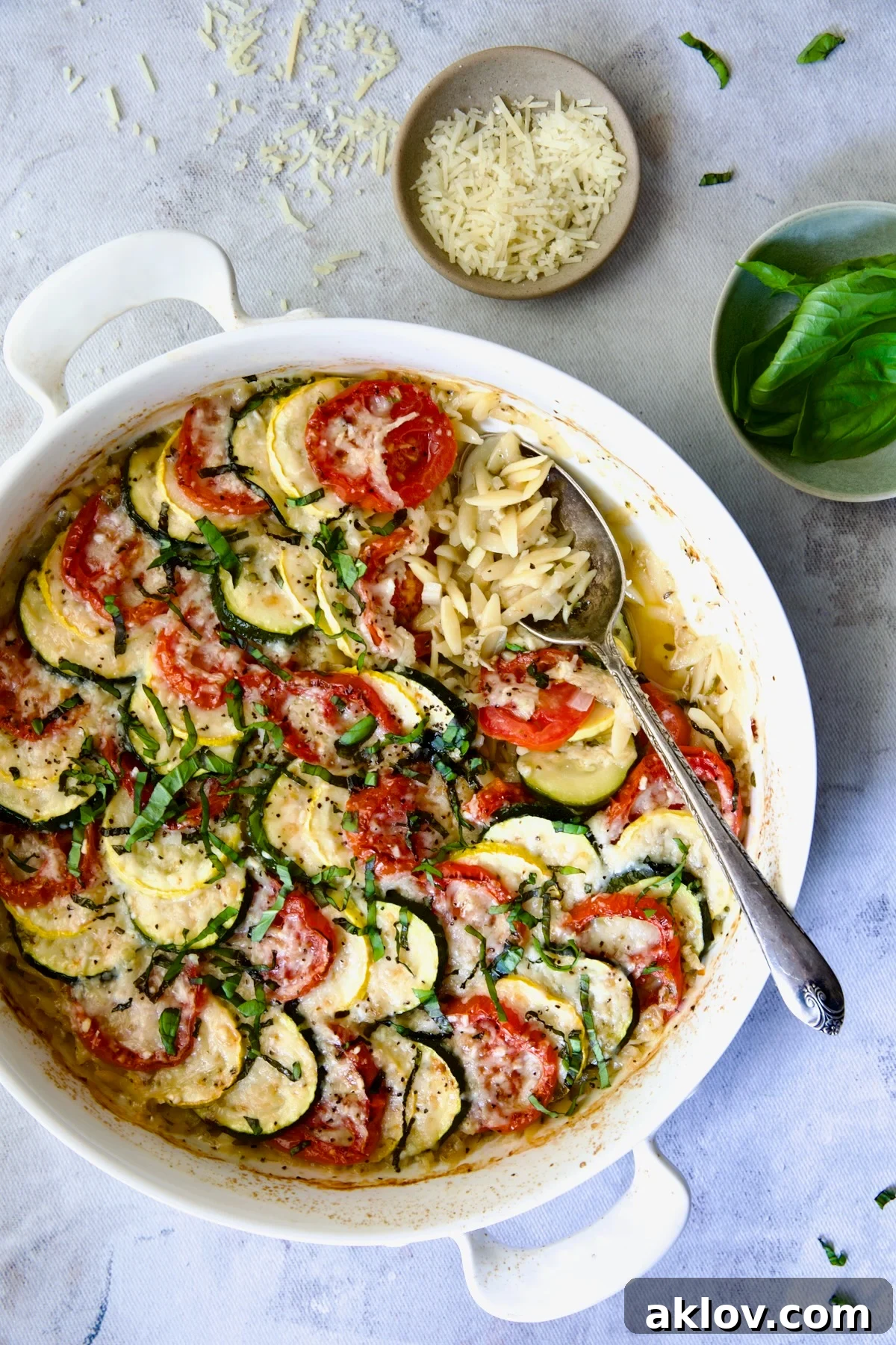 Orzo Vegetable Tian in round white baking dish with serving spoon.