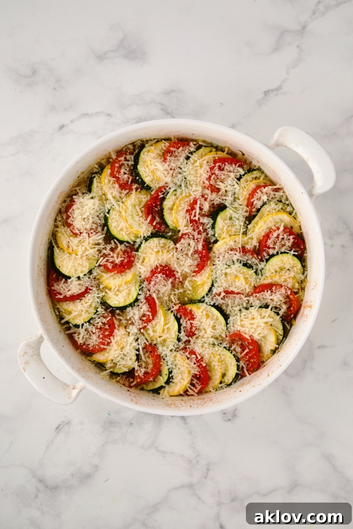 Additional Parmesan cheese being sprinkled over the baked tian before broiling.