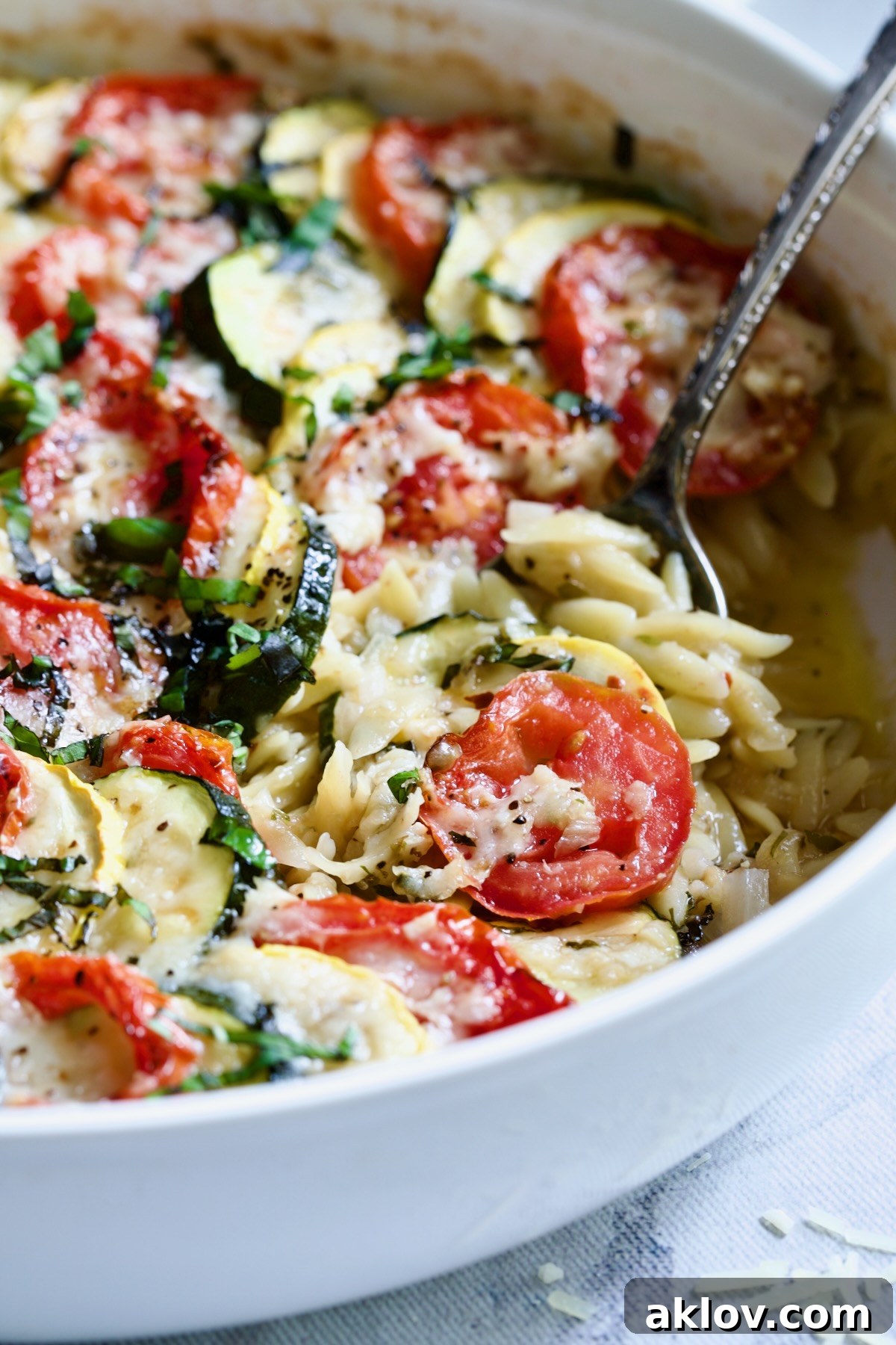 Orzo Vegetable Tian in round white baking dish with serving spoon.
