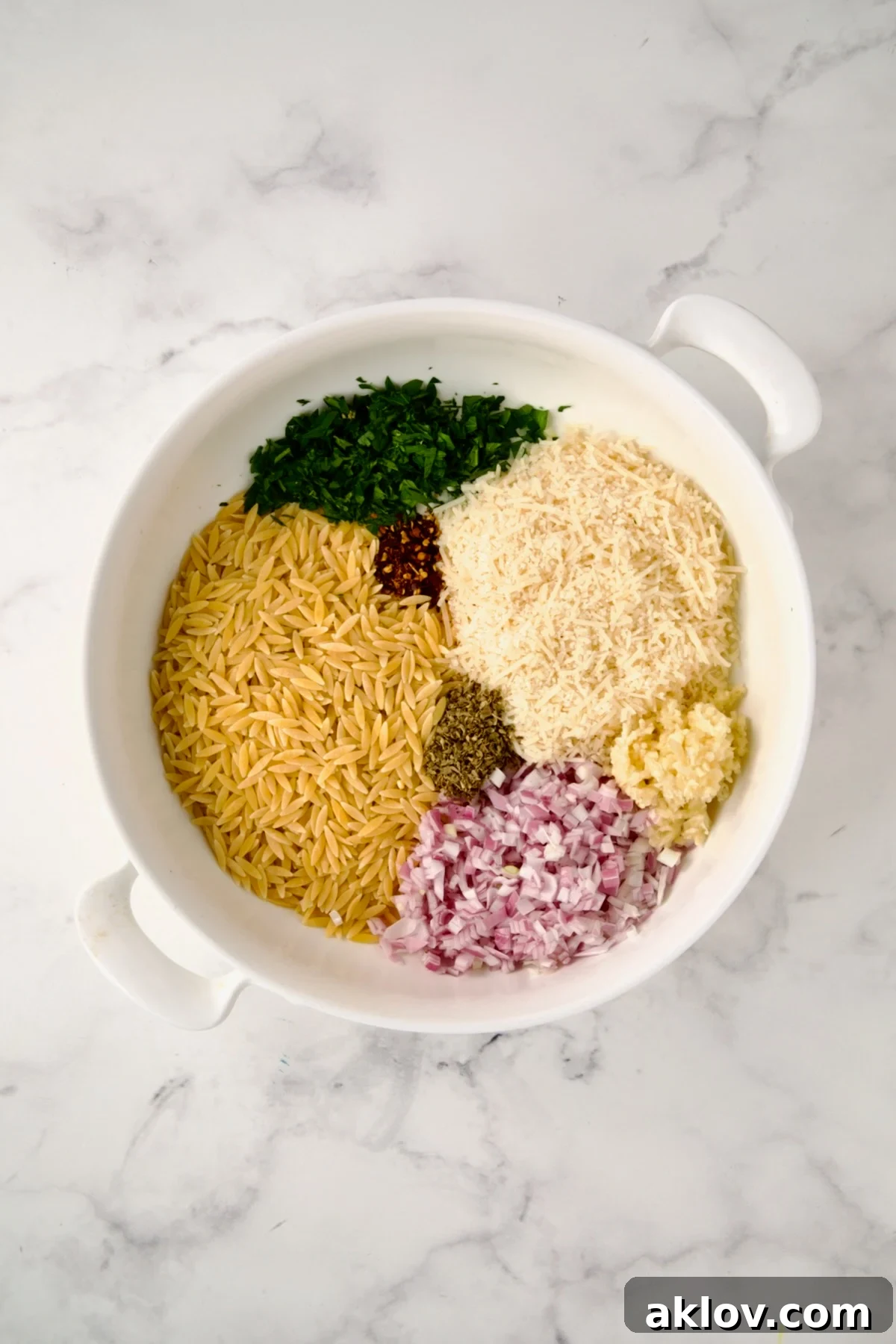 Ingredients for the tian, including orzo, cheese, and herbs, in a round white baking dish before mixing.