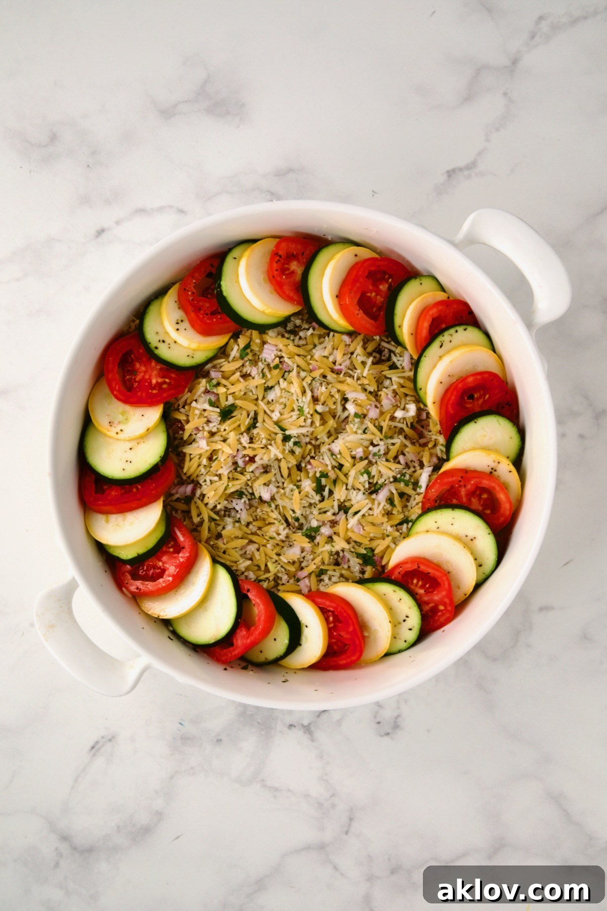 The initial layer of yellow squash, zucchini, and tomatoes arranged in a shingled pattern over the orzo.
