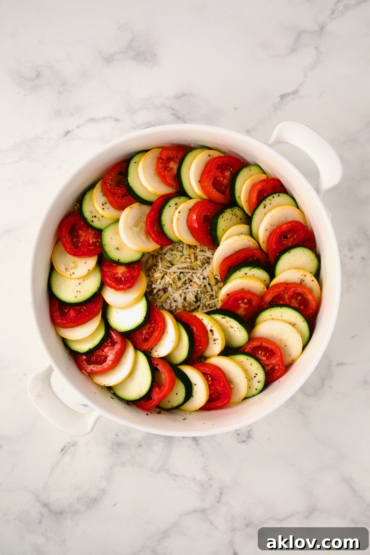 Ingredients for tian in round white baking dish with two circles of yellow squash, zucchini and tomatoes.