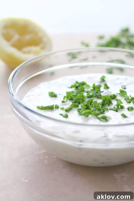 A glass mixing bowl holds creamy Lemon Chive Aioli, garnished with a sprinkle of fresh green chives, highlighting its vibrant freshness.