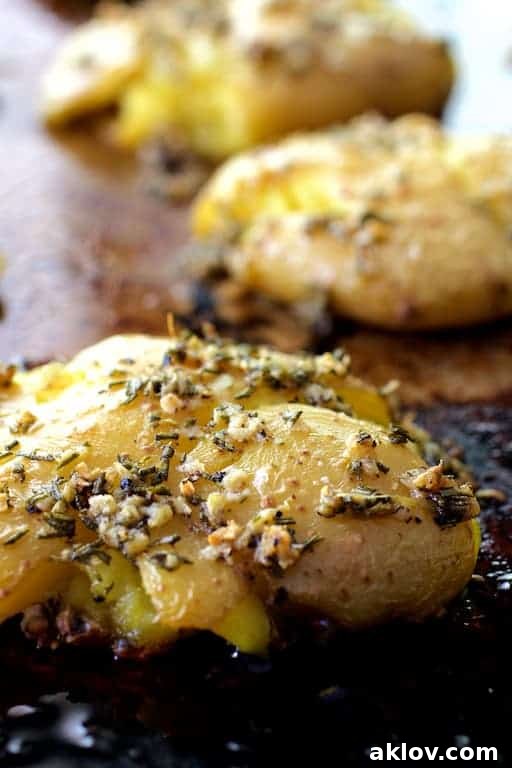 A tantalizing close-up view of Rosemary Garlic Crushed Potatoes on a baking sheet, highlighting their crispy, golden-brown skin speckled with fresh herbs and garlic.