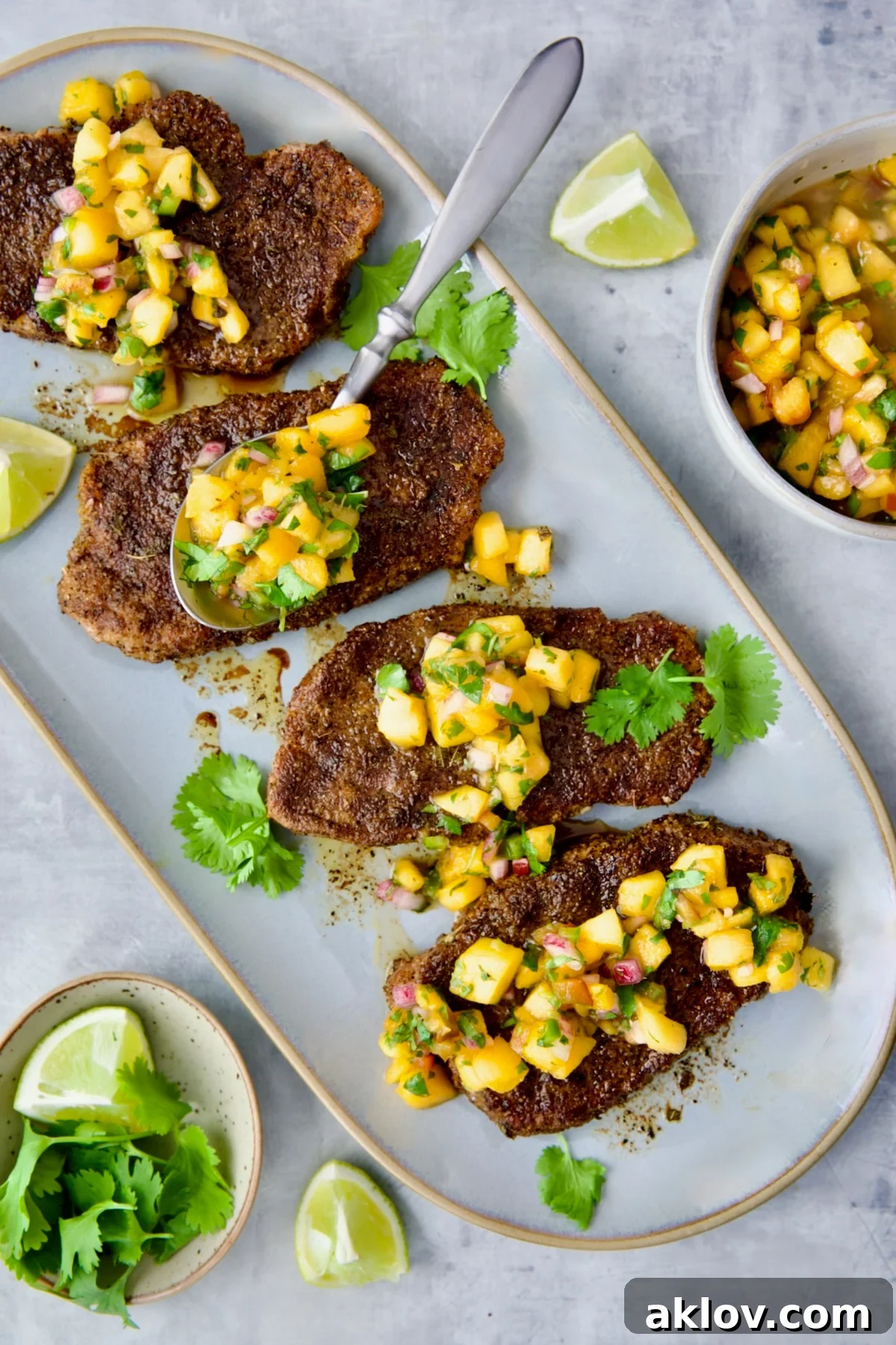Four Pork Chops with Peach Salsa on oval gray platter with spoon placing some of the salsa on each pork chop.