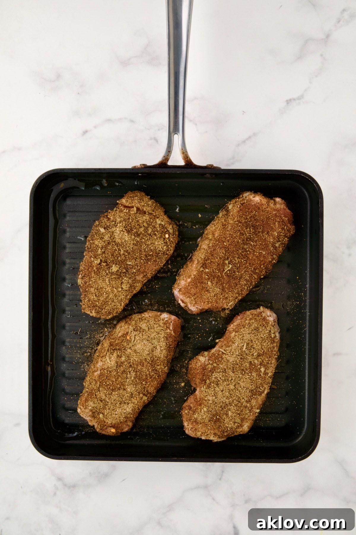 Four boneless pork chops rubbed with spice rub on square grill pan before being completely grilled.