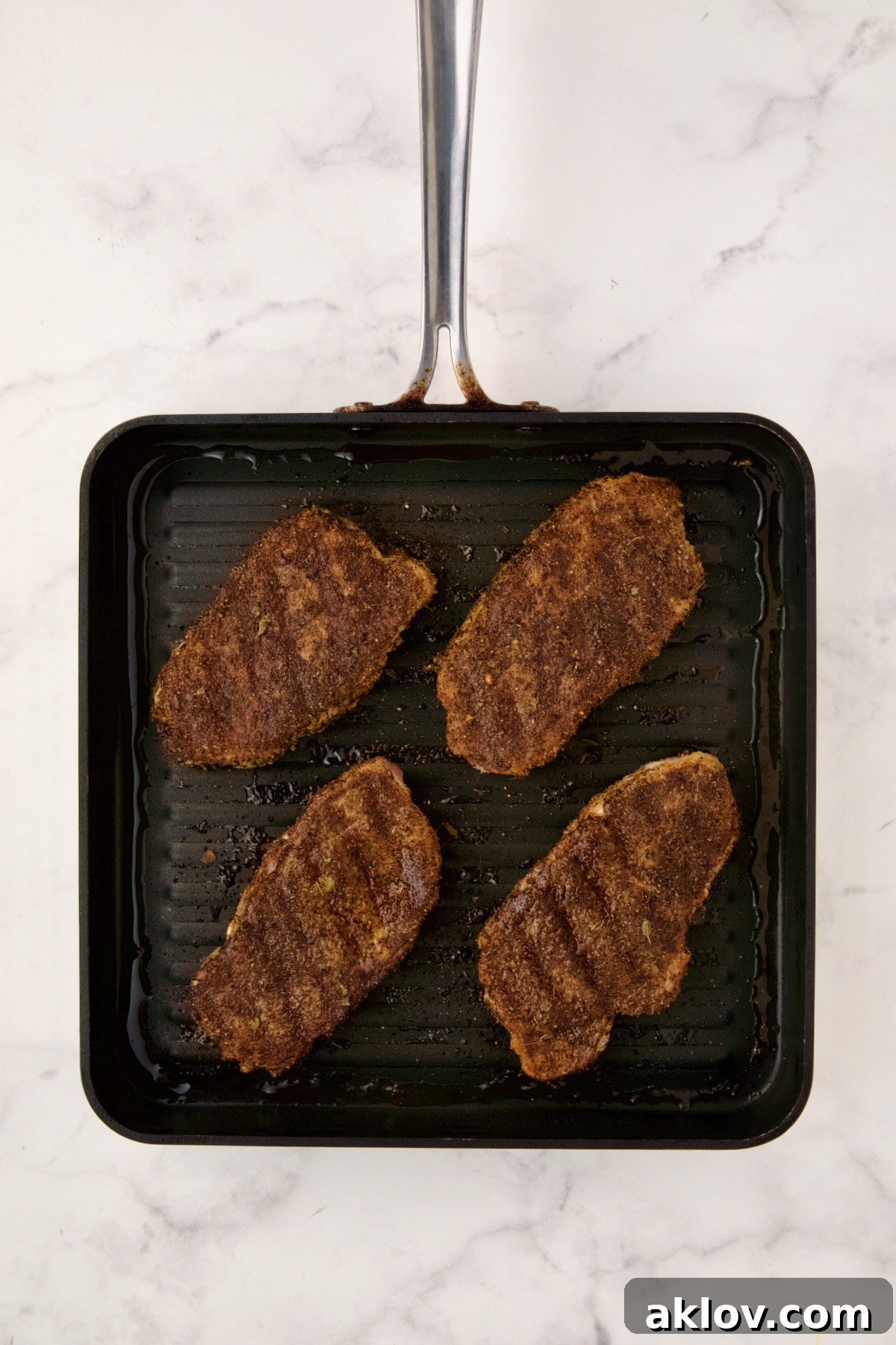 Four grilled boneless pork chops resting on a square grill pan after being fully cooked, showcasing a golden-brown exterior and distinct grill marks.