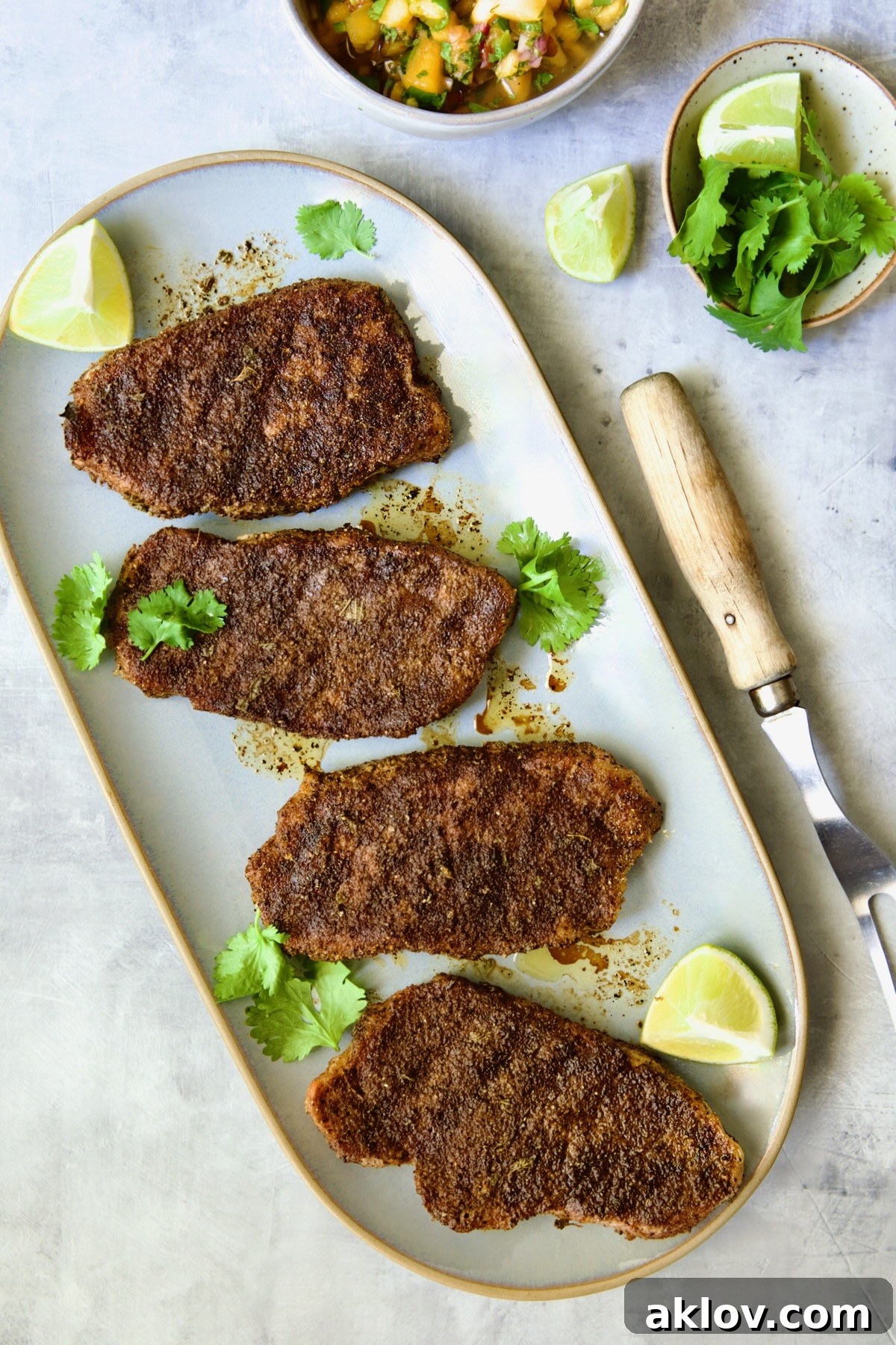 Four perfectly grilled boneless pork chops arranged on a gray oval platter, ready to be topped with the fresh peach salsa.