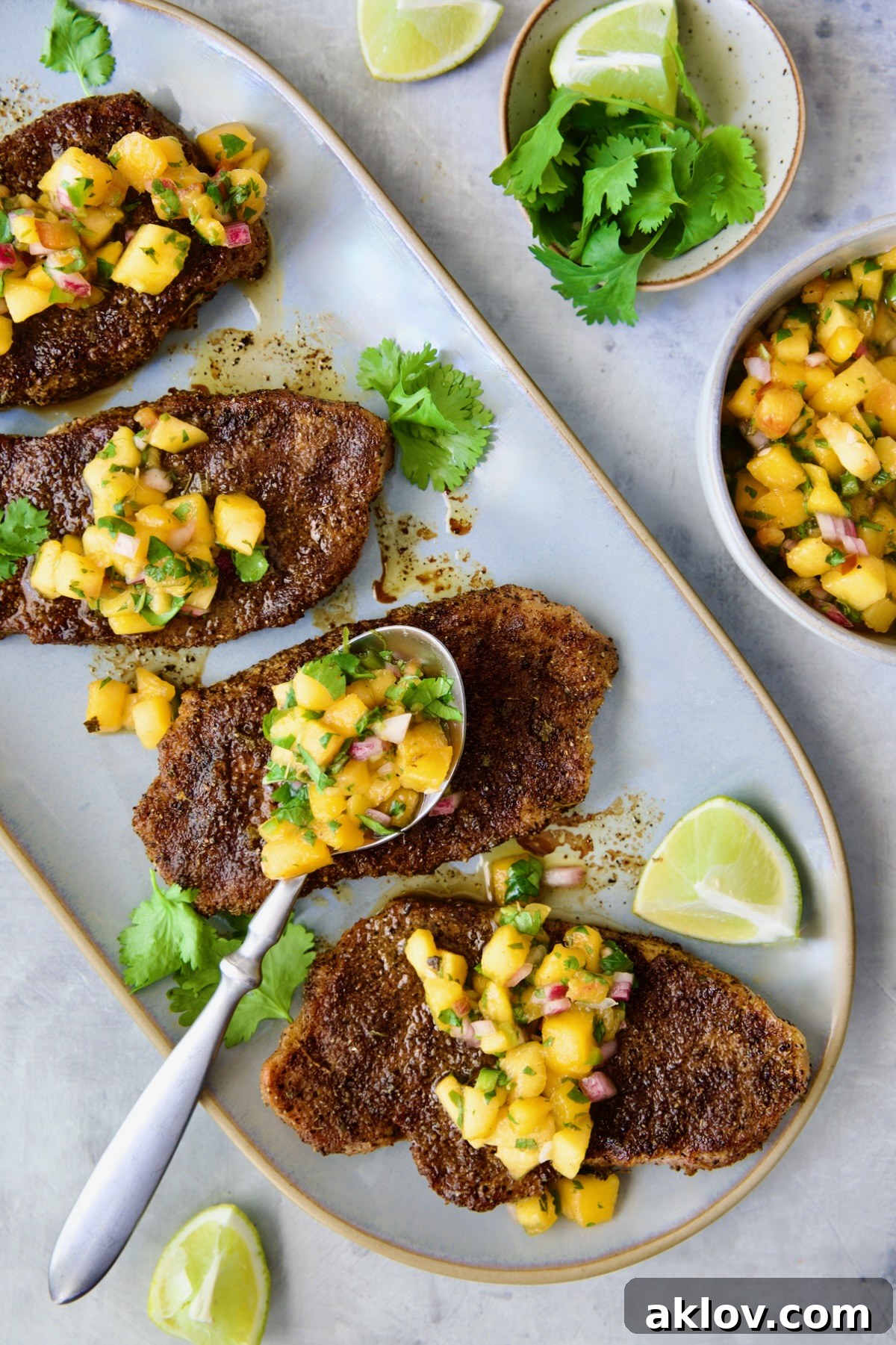 Four grilled Pork Chops with Peach Salsa on oval gray platter with salsa-filled spoon resting on one of the chops.