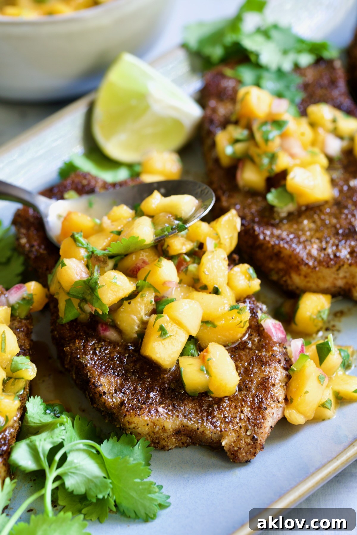 A close-up of a perfectly grilled pork chop generously topped with vibrant peach salsa, with a salsa-filled spoon resting on the chop, ready to be enjoyed.