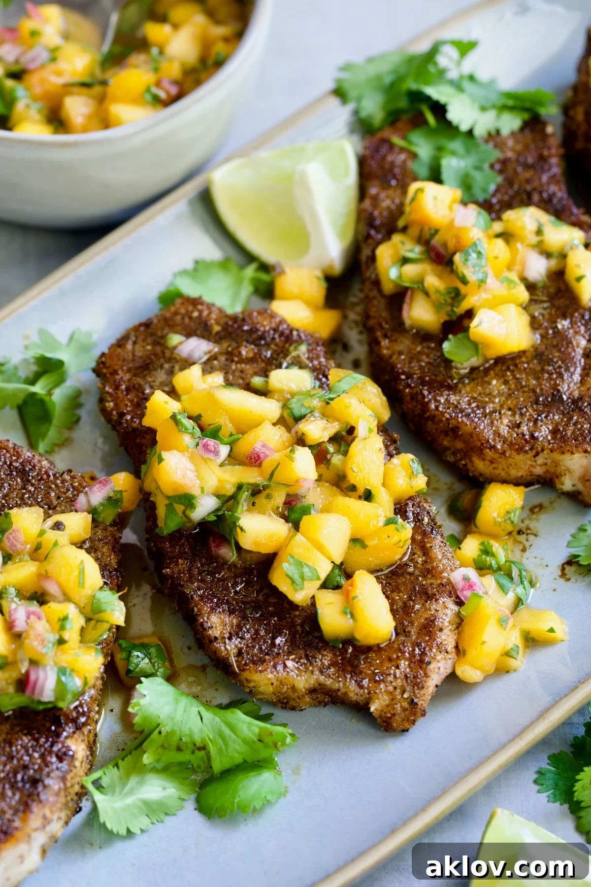Three succulent grilled pork chops, each generously topped with bright, fresh peach salsa, beautifully presented on an oval gray platter.