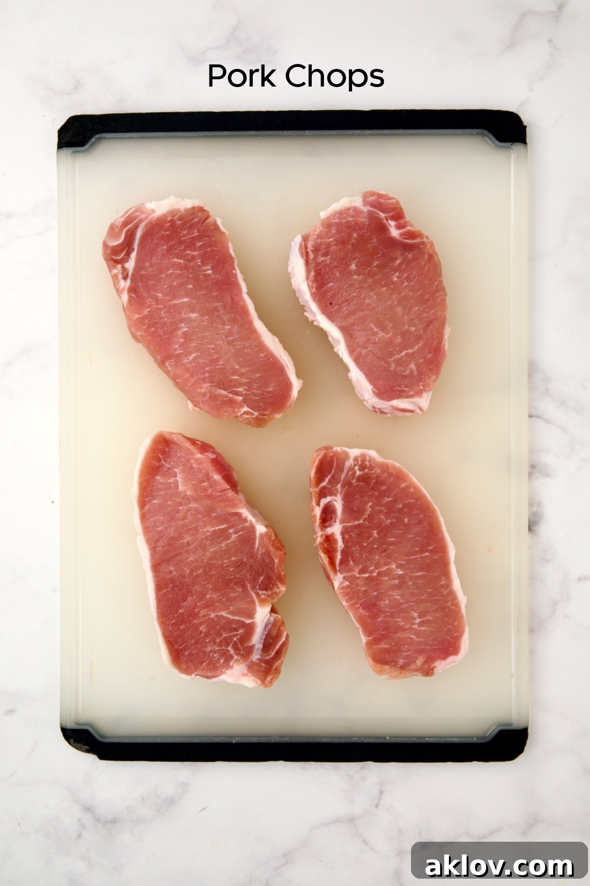 Four uncooked boneless pork chops on white plastic cutting board.