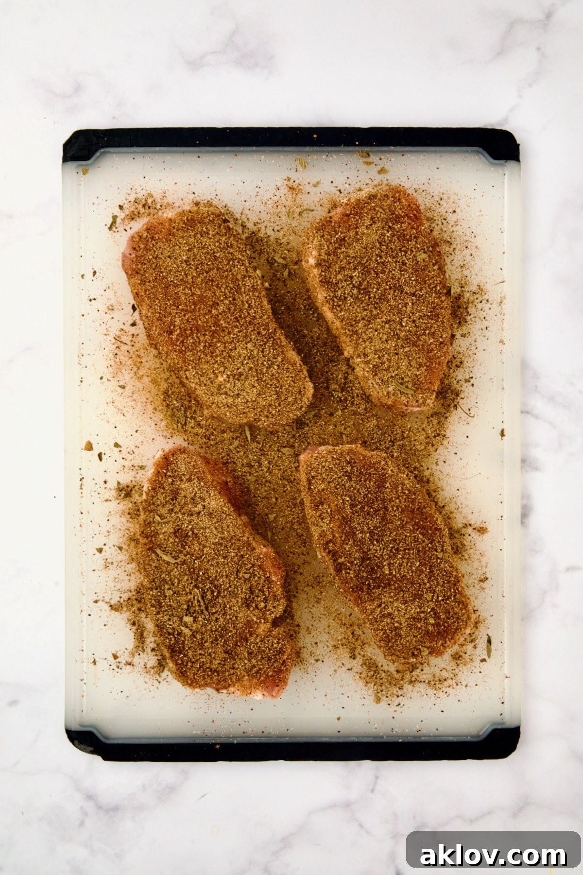 Four uncooked boneless pork chops laid on a white plastic cutting board, generously dusted and coated with the vibrant Southwestern spice rub.