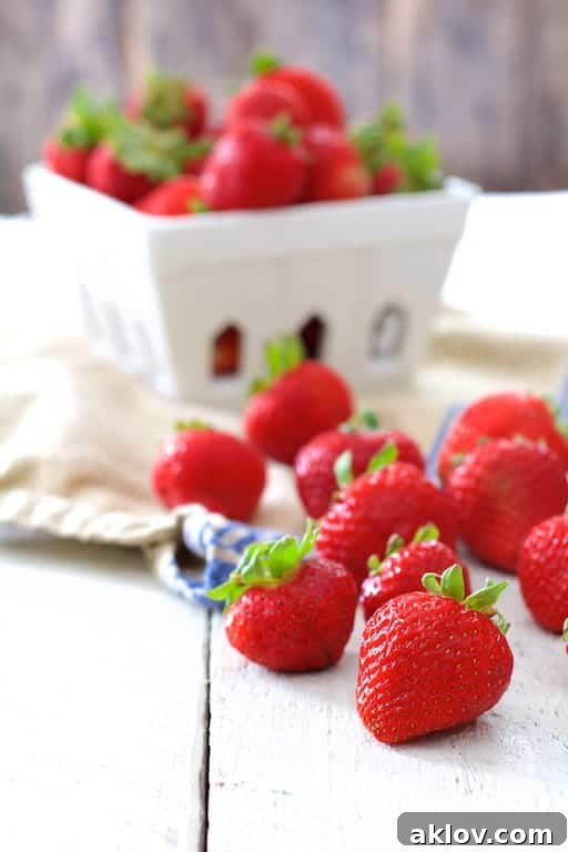 Photo of fresh berries on white painted wood surface with basket of berries in background.