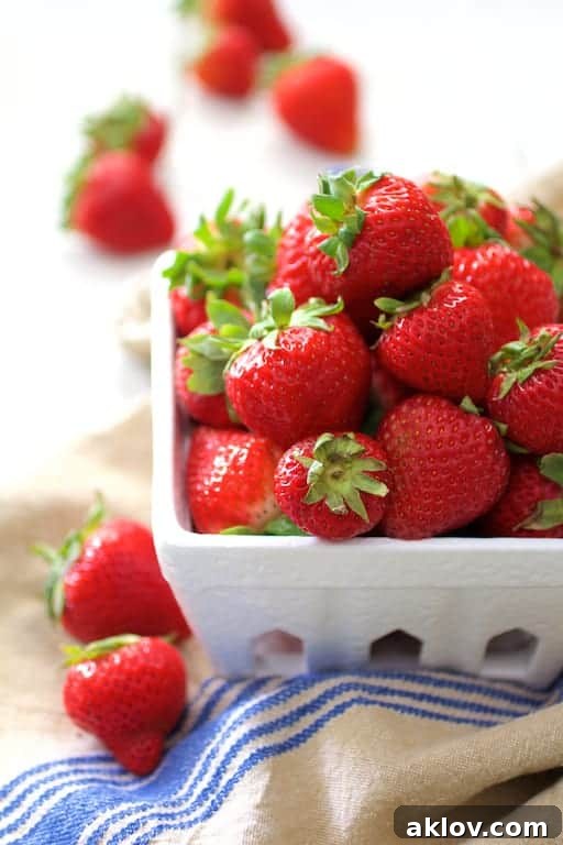 Photo of bright red, freshly picked strawberries nestled in a classic white berry basket, resting on a blue-striped towel, emphasizing their freshness and farm-to-table appeal.