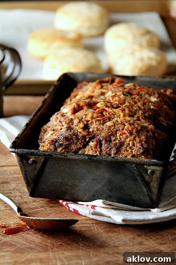 Photo of Chili Glazed Meatloaf without the glaze on top in aged loaf pan with biscuits in the background.