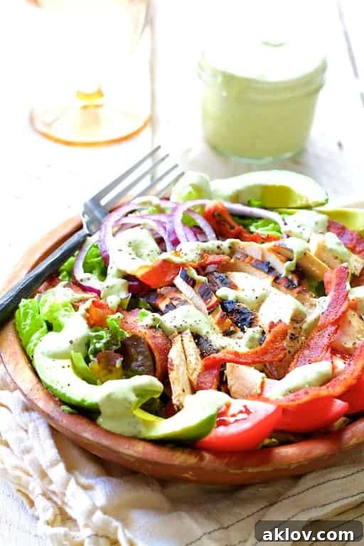 Chicken BLT Salad with Spicy Avocado Ranch Dressing in a wood bowl, with dressing on the side and a water glass in the background on a beige napkin.