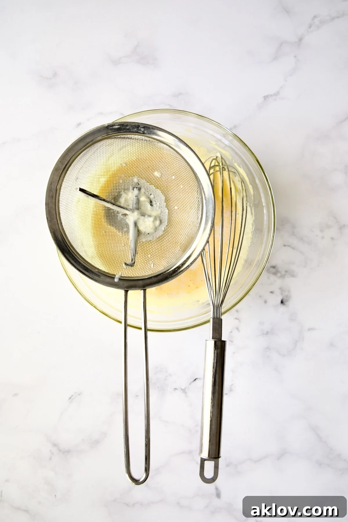 A fine-mesh sieve in action, straining the vanilla-infused cream mixture into the beaten egg yolks and sugar.