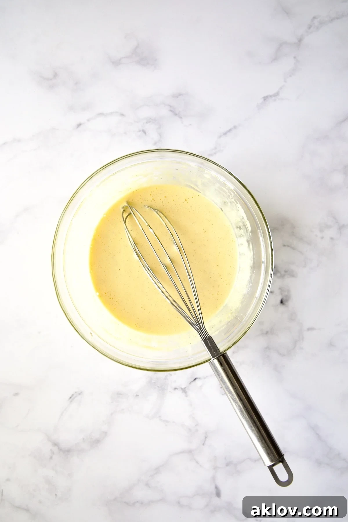 Smooth crème brûlée batter, with a whisk resting in a glass bowl, signaling it's ready for baking.