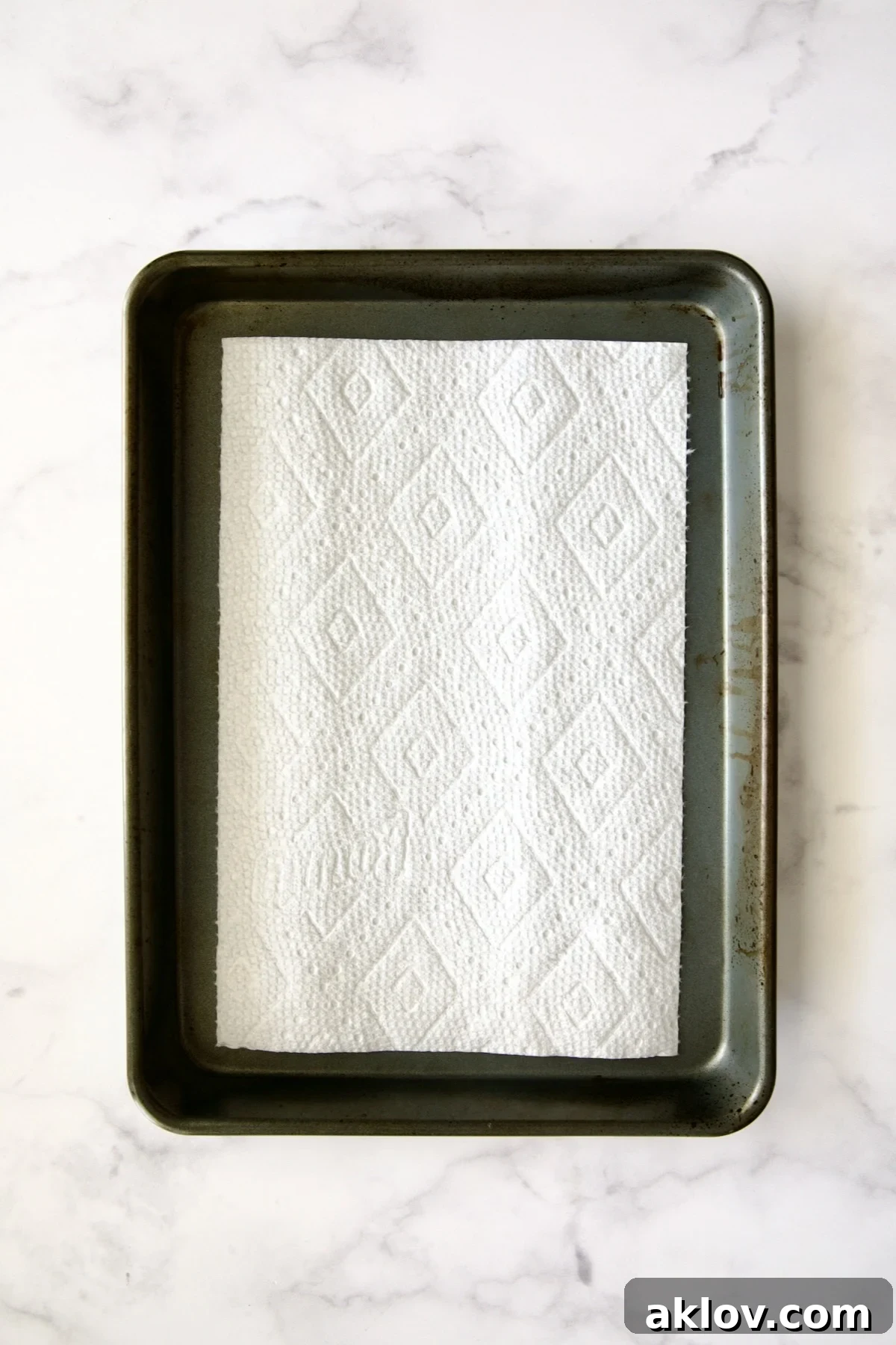 A dry piece of paper towel meticulously placed on the bottom of a rimmed sheet pan, ready for ramekins.