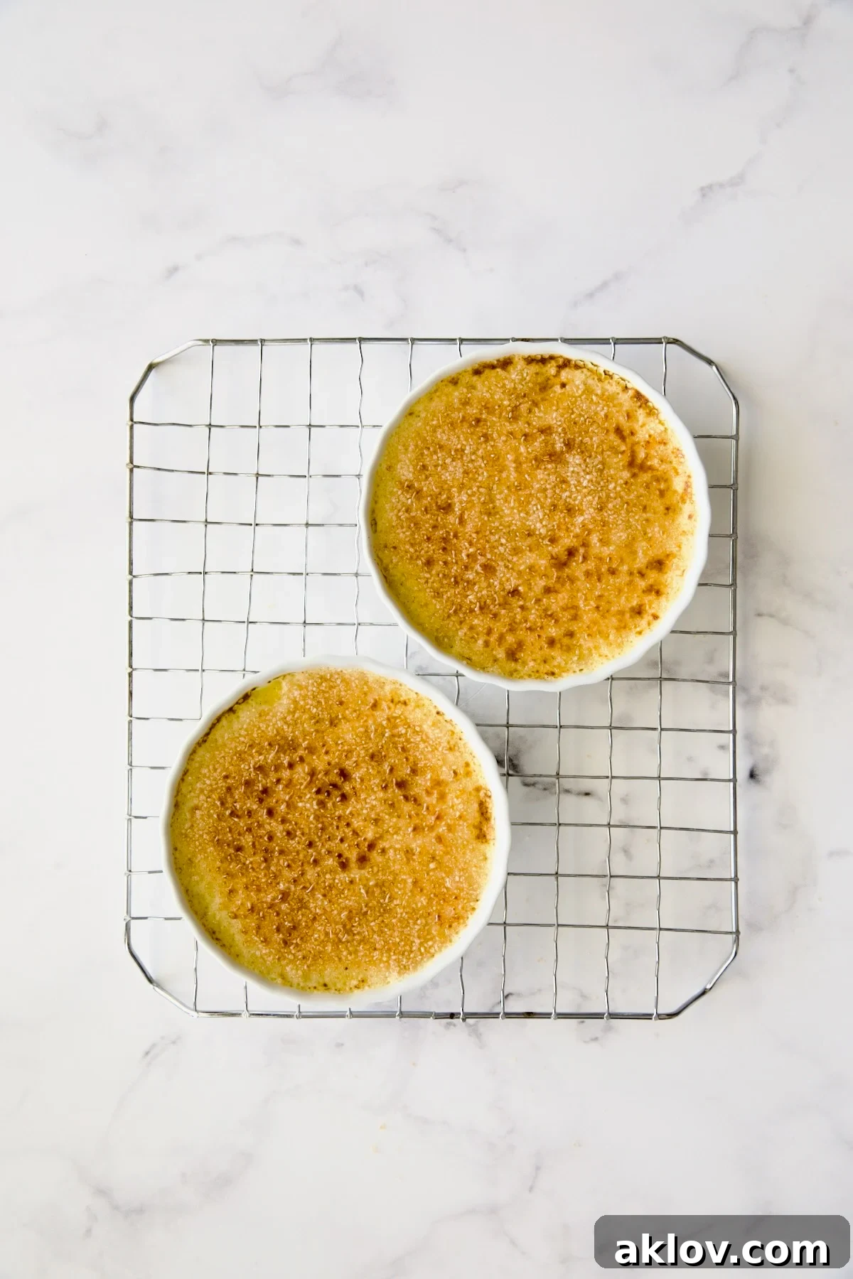 Two perfectly caramelized Classic Crème Brûlées, featuring glossy, hardened sugar crusts, cooling on a wire rack.
