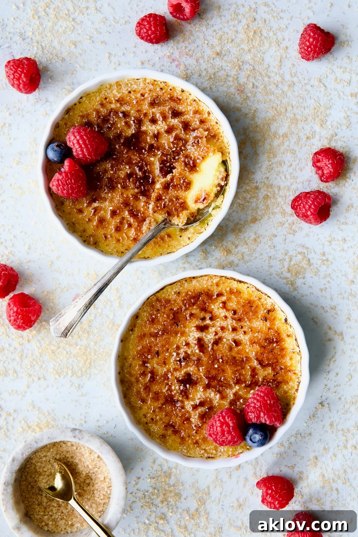 Two dishes of Classic Crème Brûlée for Two, artfully garnished with vibrant red raspberries and succulent blueberries.