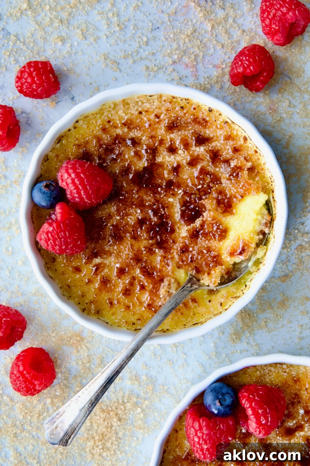 A single dish of Classic Crème Brûlée for Two, beautifully garnished with red raspberries and blueberries, ready to be enjoyed.